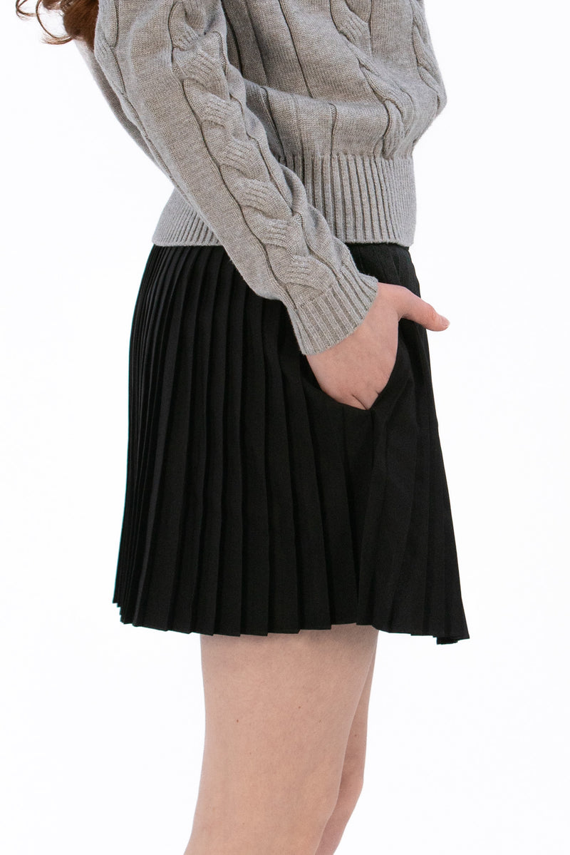 Woman wearing a gray cable knit sweater and Black pleated skirt