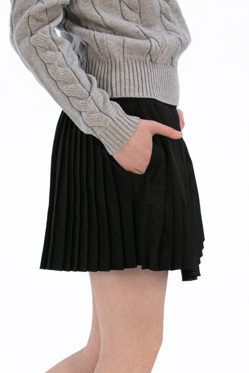 Woman wearing a gray cable knit sweater and Black pleated skirt