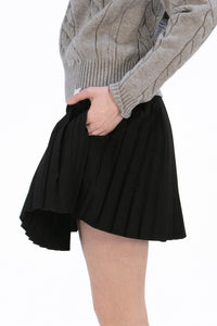 Woman wearing a gray cable knit sweater and Black pleated skirt