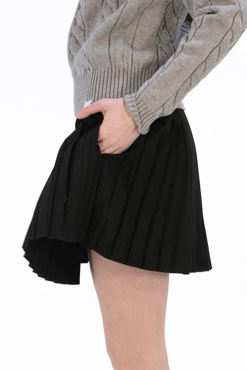Woman wearing a gray cable knit sweater and Black pleated skirt