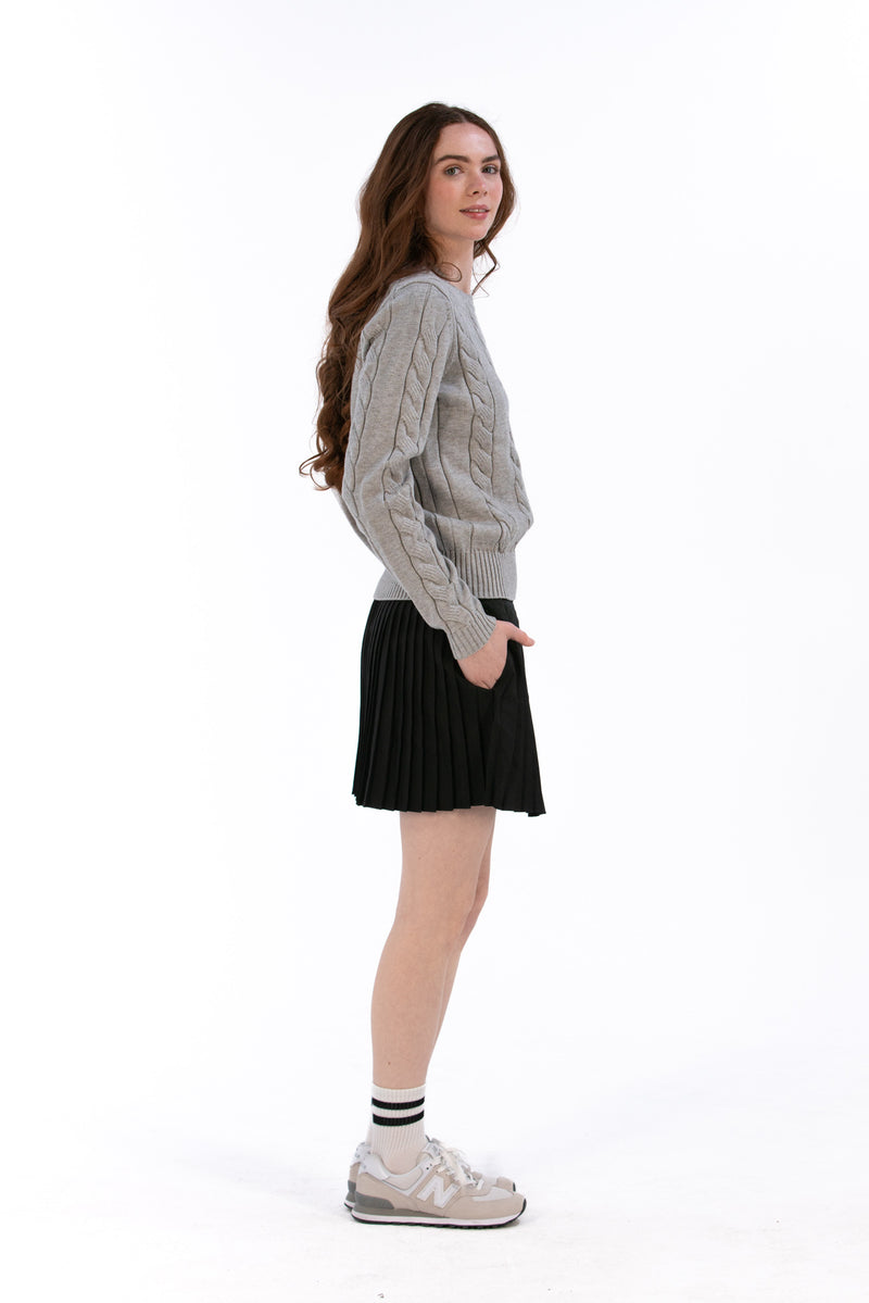 Woman wearing a gray cable knit sweater and Black pleated skirt