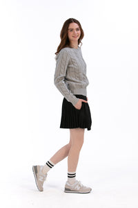 Woman wearing a gray cable knit sweater and Black pleated skirt