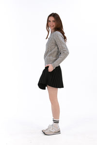 Woman wearing a gray cable knit sweater and Black pleated skirt