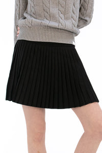 Woman wearing a gray cable knit sweater and Black pleated skirt
