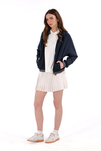 Person wearing a Navy/White bomber jacket, white shirt, pleated skirt, and white sneakers on a white background