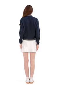 Person wearing a Navy/White bomber jacket, white shirt, pleated skirt, and white sneakers on a white background