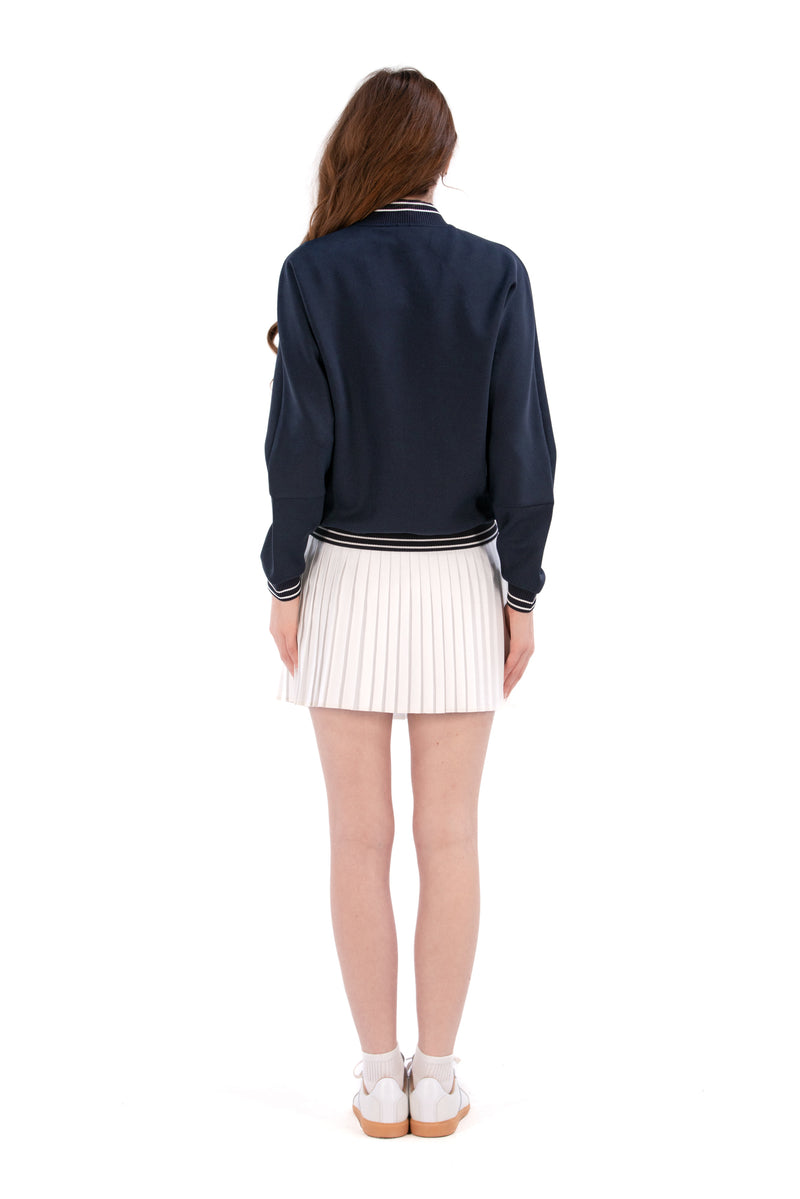 Person wearing a Navy/White bomber jacket, white shirt, pleated skirt, and white sneakers on a white background