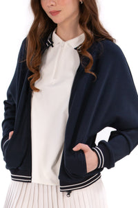 Person wearing a Navy/White bomber jacket, white shirt, pleated skirt, and white sneakers on a white background