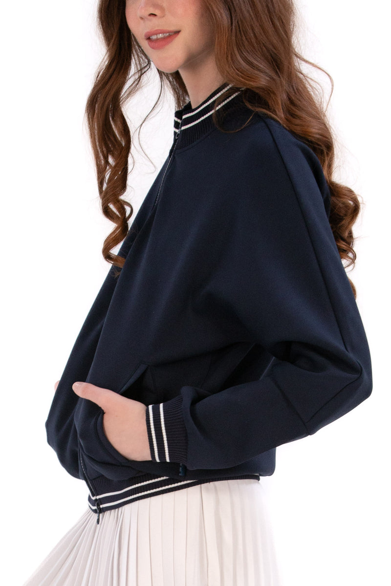 Person wearing a Navy/White bomber jacket, white shirt, pleated skirt, and white sneakers on a white background