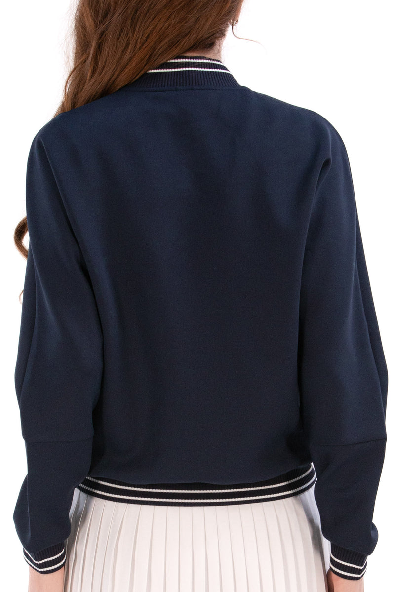 Person wearing a Navy/White bomber jacket, white shirt, pleated skirt, and white sneakers on a white background