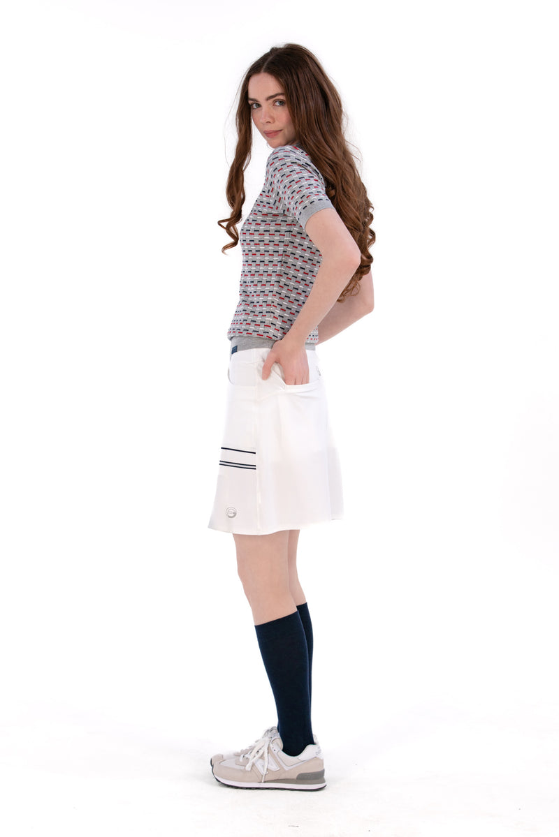 Woman wearing a Grey/Navy/Red patterned shirt, white shorts, and black socks on a white background