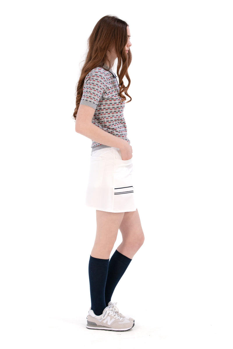 Woman wearing a Grey/Navy/Red patterned shirt, white shorts, and black socks on a white background