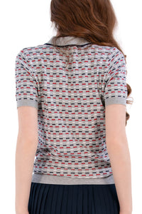 Woman wearing a Grey/Navy/Red patterned shirt, white shorts, and black socks on a white background