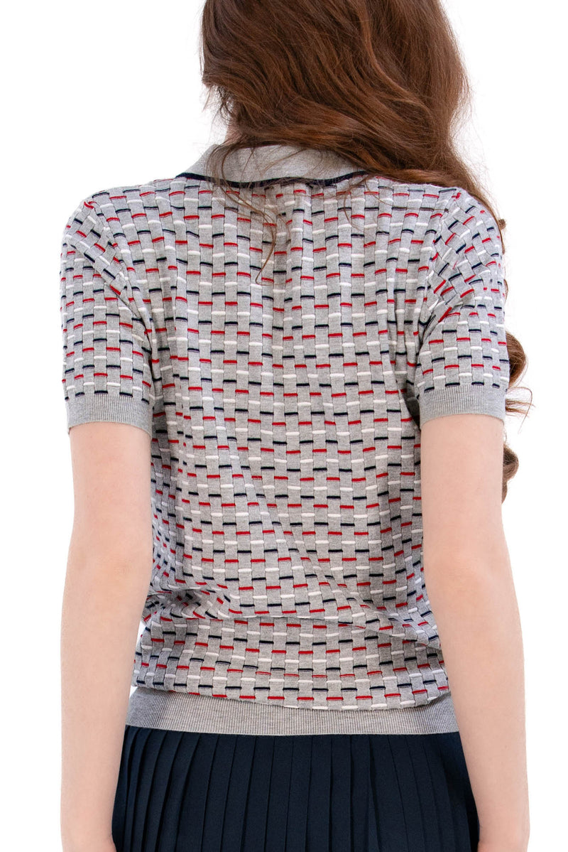 Woman wearing a Grey/Navy/Red patterned shirt, white shorts, and black socks on a white background