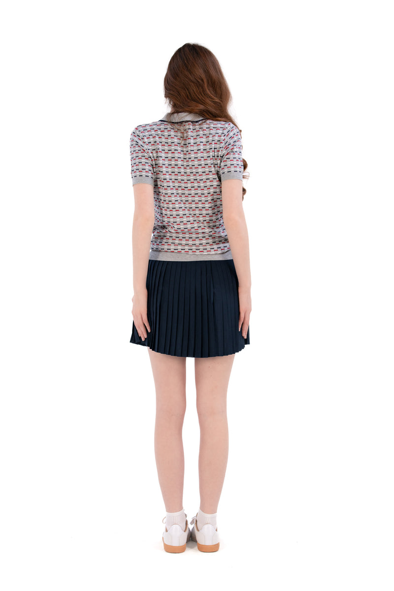 Woman wearing a Grey/Navy/Red patterned shirt, white shorts, and black socks on a white background