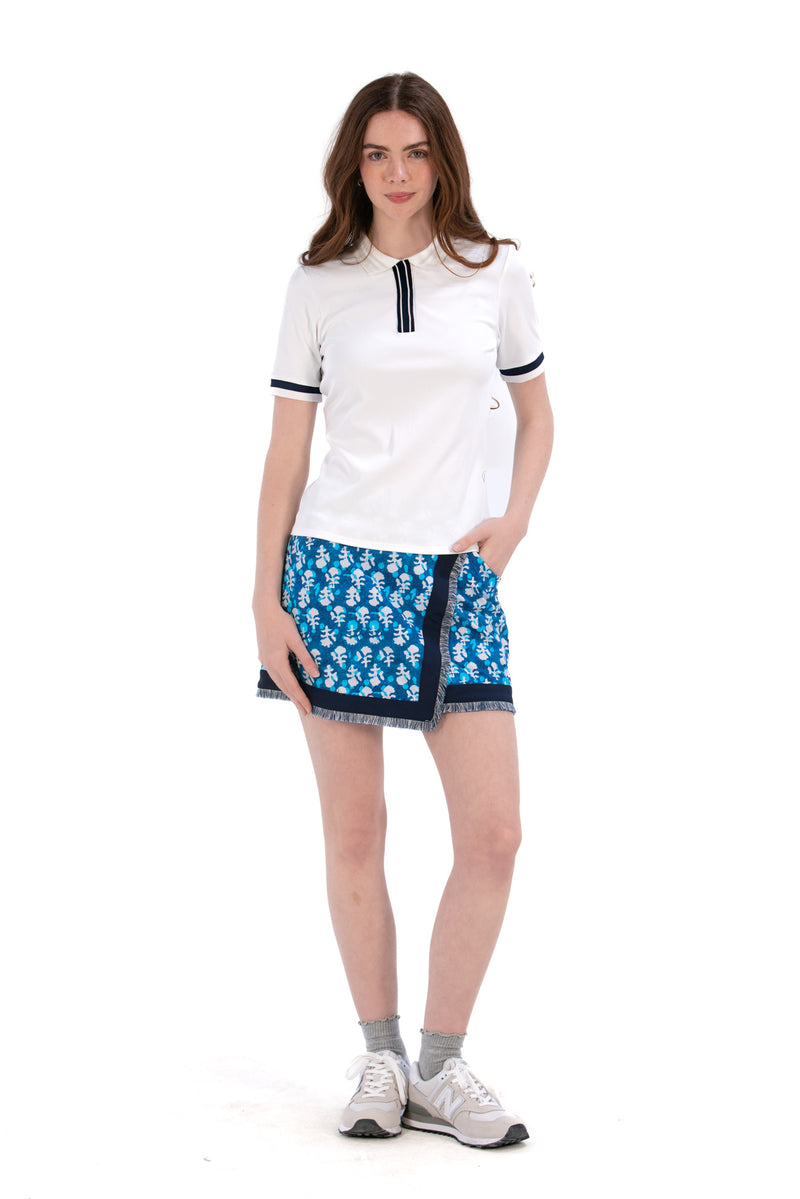 Woman wearing a white polo top and Indigo Floral patterned skirt on a white background