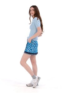 Woman wearing a blue knit polo top and Indigo Floral patterned skirt on a white background