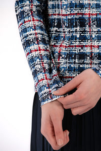 Woman wearing a Red White Blue Plaid shirt and navy pleated skirt on a white background