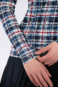 Woman wearing a Red White Blue Plaid shirt and navy pleated skirt on a white background