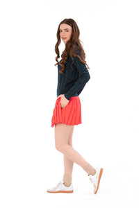 Woman wearing a navy sweater and coral pleated skirt on a white background