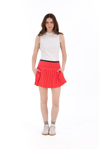 Woman wearing a white sleeveless top and coral pleated skirt on a white background