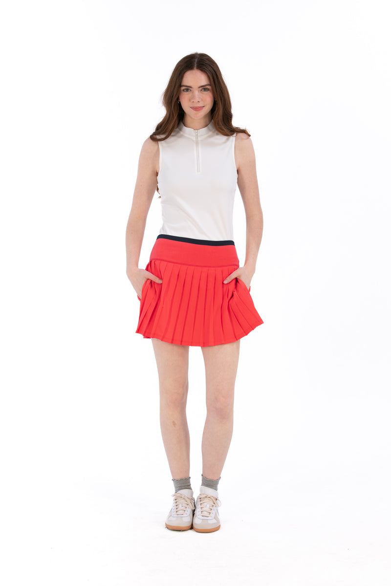 Woman wearing a white sleeveless top and coral pleated skirt on a white background