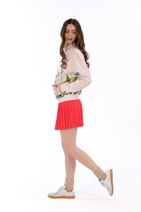 Woman wearing a floral sweater and coral pleated skirt on a white background