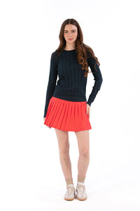 Woman wearing a navy sweater and coral pleated skirt on a white background