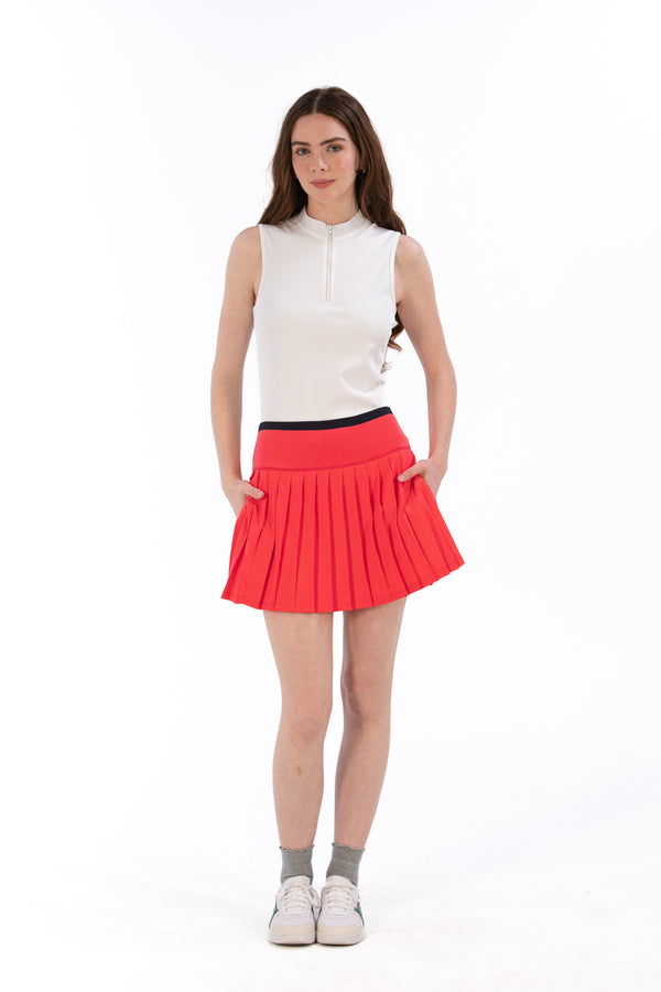 Woman wearing a white sleeveless top and coral pleated skirt on a white background