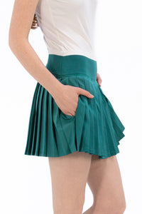 Woman wearing a white sleeveless top and Deep Jade pleated skirt on a white background