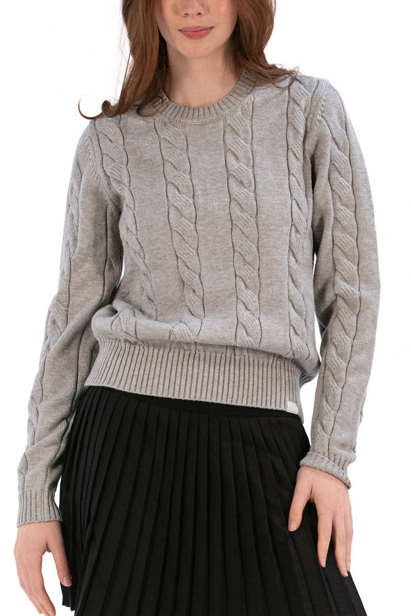 Woman wearing a marl gray cable knit sweater and black pleated skirt on a white background