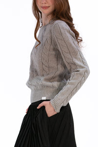 Woman wearing a marl gray cable knit sweater and black pleated skirt on a white background