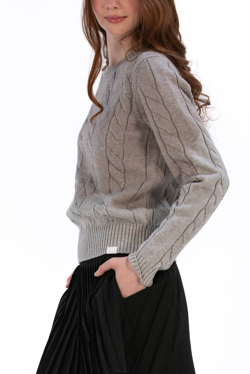 Woman wearing a marl gray cable knit sweater and black pleated skirt on a white background