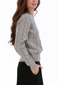Woman wearing a marl gray cable knit sweater and black pleated skirt on a white background