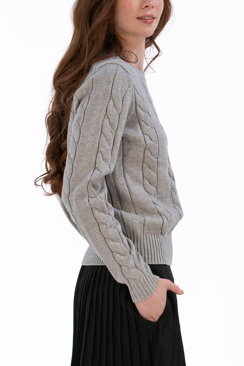 Woman wearing a marl gray cable knit sweater and black pleated skirt on a white background