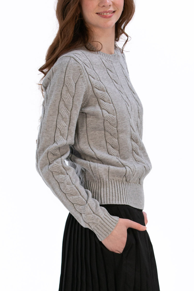 Woman wearing a marl gray cable knit sweater and black pleated skirt on a white background