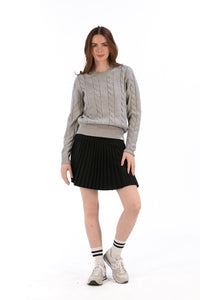 Woman wearing a marl gray cable knit sweater and black pleated skirt on a white background