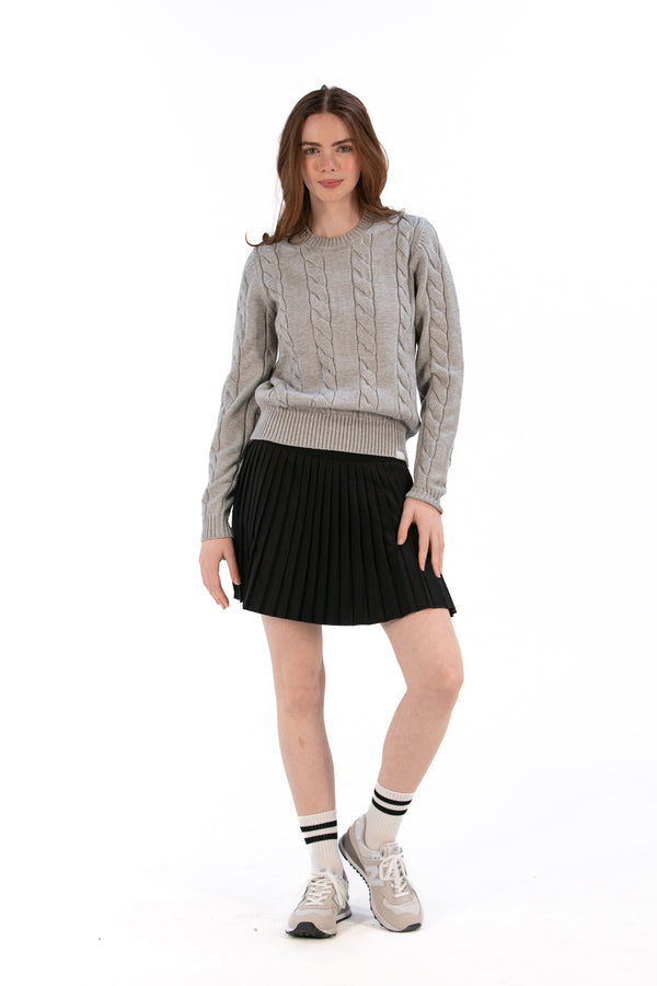 Woman wearing a marl gray cable knit sweater and black pleated skirt on a white background
