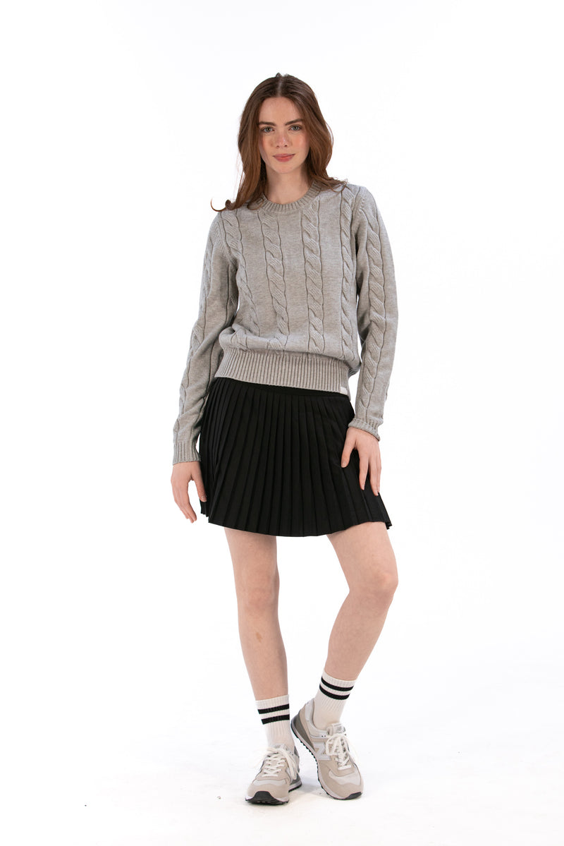 Woman wearing a marl gray cable knit sweater and black pleated skirt on a white background