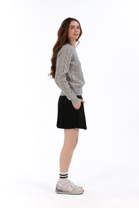 Woman wearing a marl gray cable knit sweater and black pleated skirt on a white background