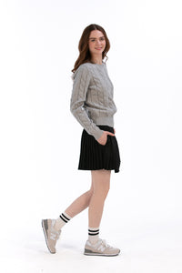 Woman wearing a marl gray cable knit sweater and black pleated skirt on a white background