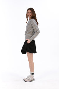 Woman wearing a marl gray cable knit sweater and black pleated skirt on a white background