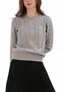 Woman wearing a marl gray cable knit sweater and black pleated skirt on a white background