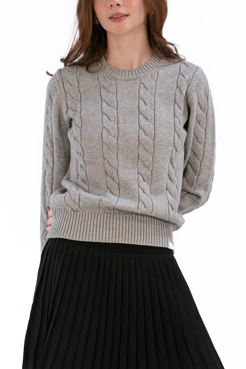 Woman wearing a marl gray cable knit sweater and black pleated skirt on a white background