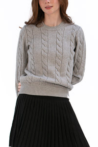 Woman wearing a marl gray cable knit sweater and black pleated skirt on a white background