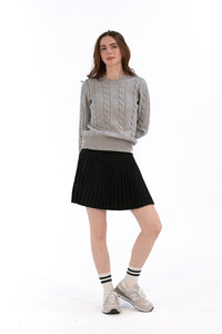 Woman wearing a marl gray cable knit sweater and black pleated skirt on a white background