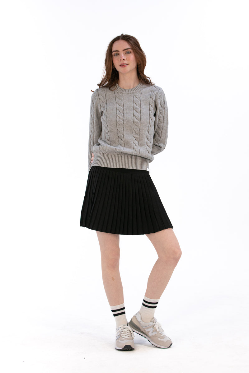 Woman wearing a marl gray cable knit sweater and black pleated skirt on a white background