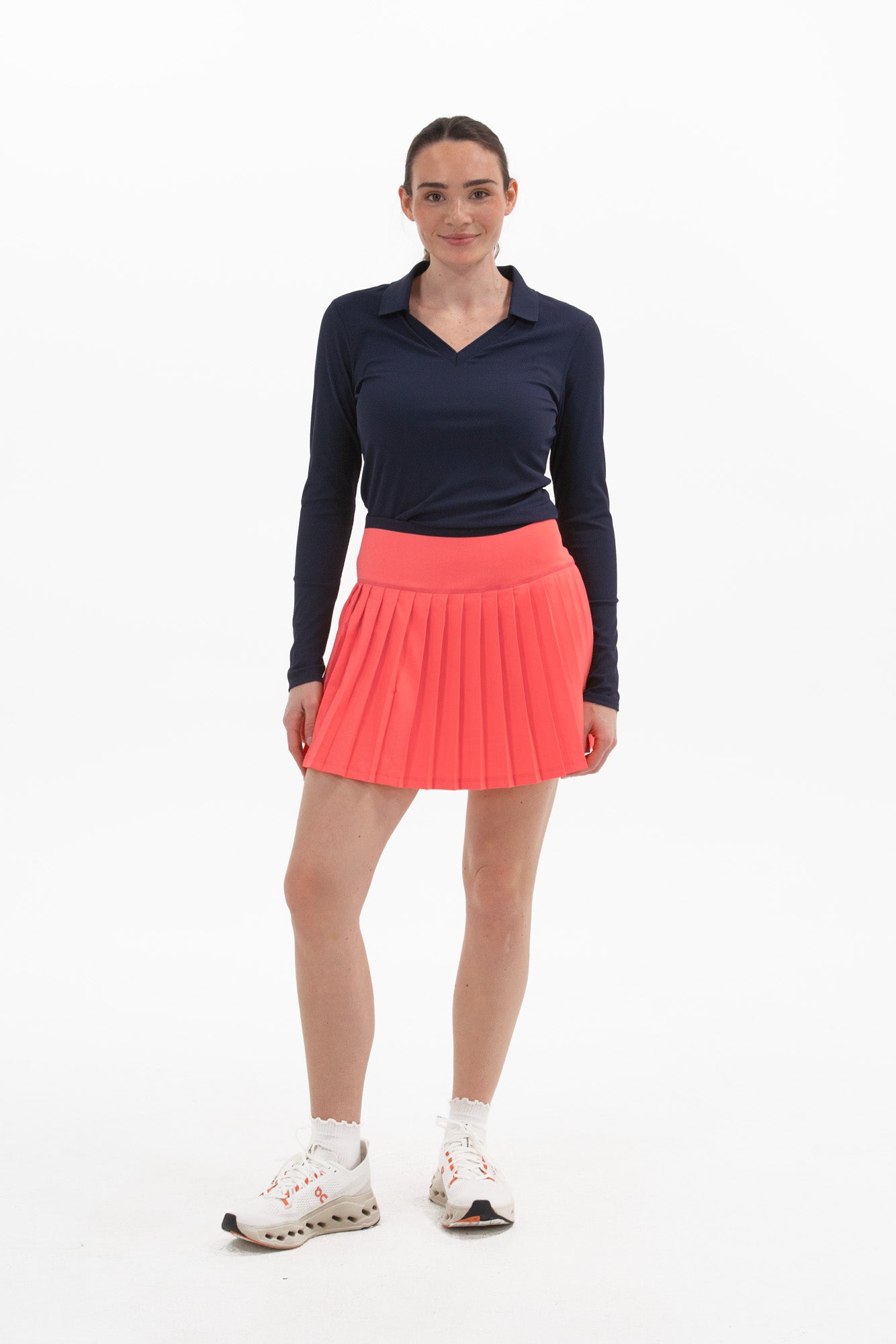 Woman wearing a navy long-sleeve top and coral pleated skirt on a white background - Coral